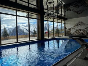 A swimming pool with a view of snow-capped mountains through large windows.