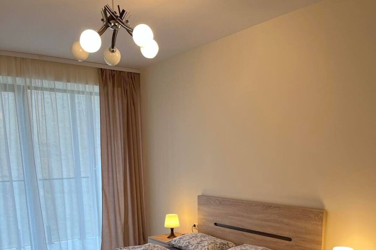 A bedroom with a large bed, two bedside tables with lamps, a wooden headboard, and a ceiling light fixture.