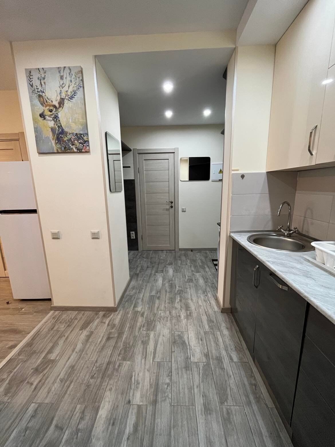 A modern kitchen with grey wooden flooring, white cabinets, and a stainless steel sink.