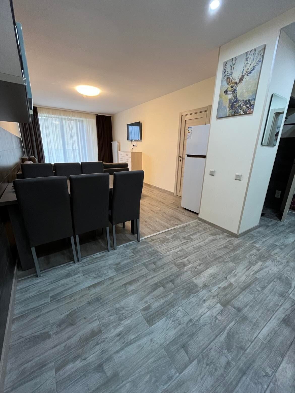 A modern kitchen with a dining area, a TV mounted on the wall, and a refrigerator.