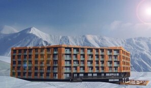 A modern building with a grid of windows and a flat roof, situated on a snowy landscape with mountains in the background.