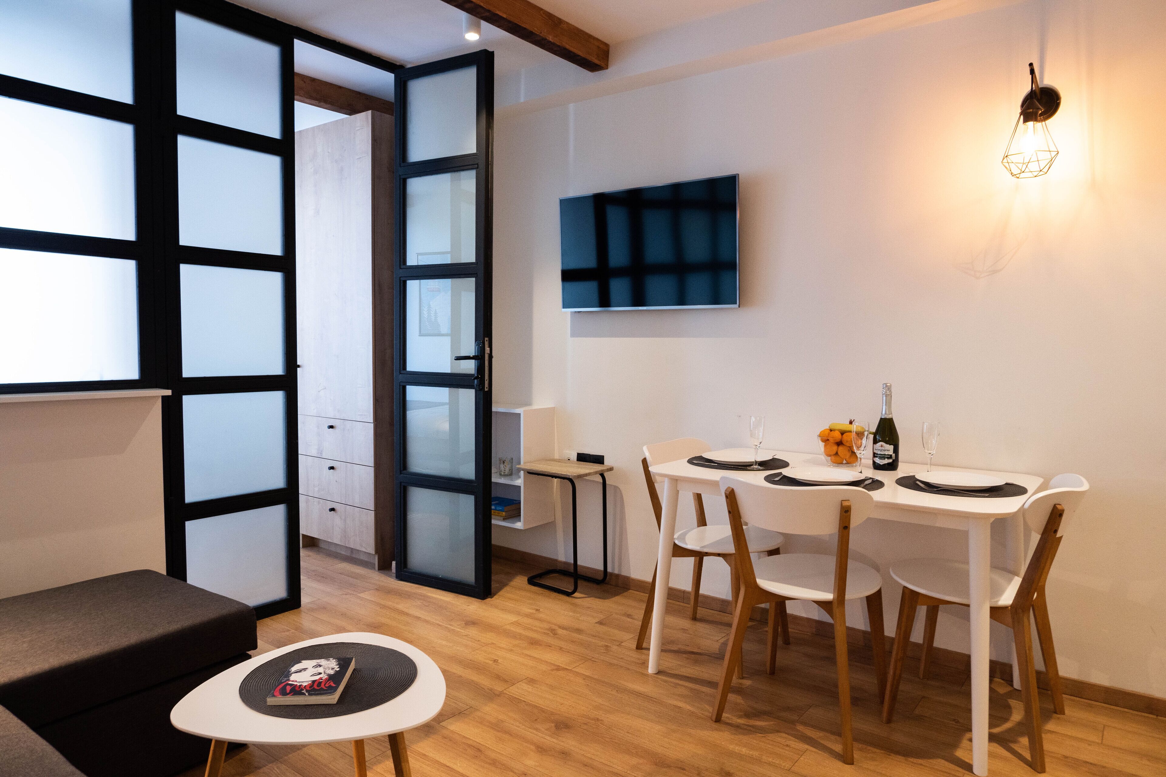 Uma sala de jantar moderna com uma mesa posta para dois, um sofá e uma pequena mesa lateral com um livro.