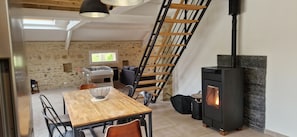 A loft-style room with a wooden dining table, chairs, a ladder, a fireplace, and a stone wall. - Gîte Dune between orchard and Omaha beach (Colleville sur mer)