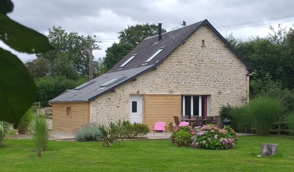 A stone house with a sloped roof, a wooden door, and a small porch with two chairs. - Gîte Dune between orchard and Omaha beach (Colleville sur mer)