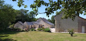 A row of stone buildings with pitched roofs, surrounded by a grassy area and trees. - Gîte Dune between orchard and Omaha beach (Colleville sur mer)