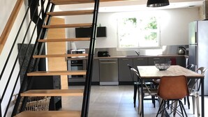 A modern kitchen with a dining area, a staircase, and a window. - Gîte Dune between orchard and Omaha beach (Colleville sur mer)