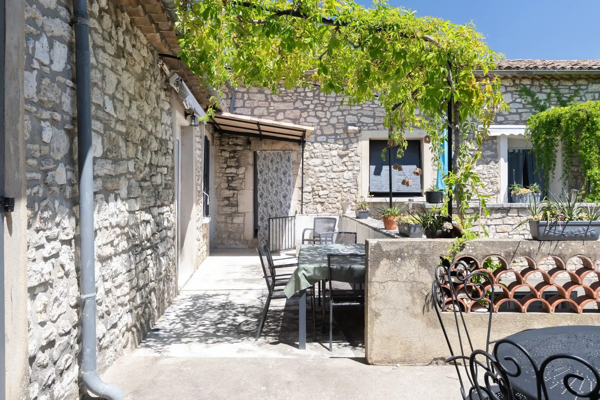 A stone building with a covered outdoor seating area, including a table and chairs, and potted plants.