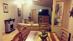 A dining area with a wooden table, chairs, and a bowl of fruit. There is a sofa and a television in the background. - Location!  Nice log home in dark sky community next to several peaks (Westcliffe)