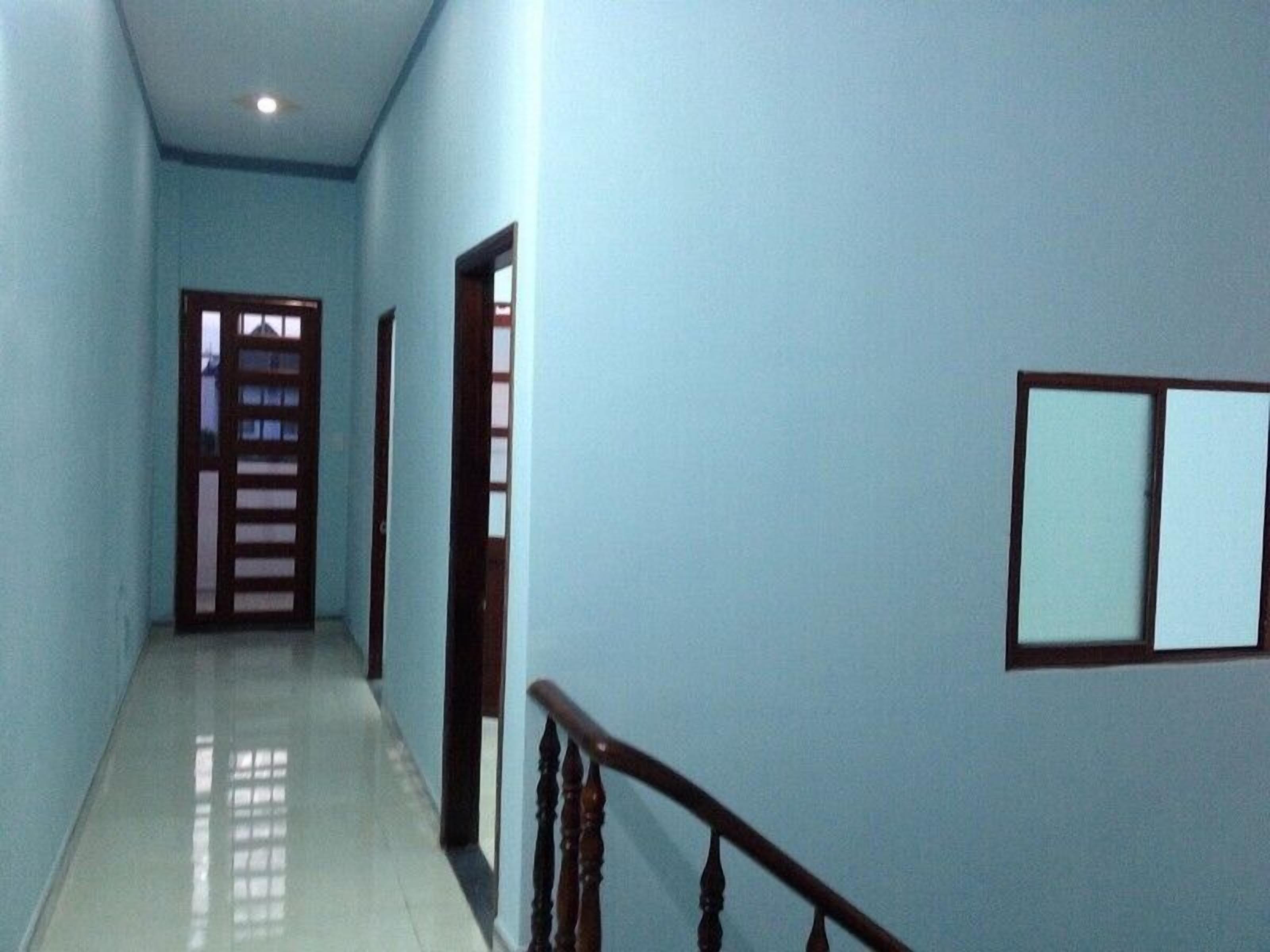 A narrow hallway with light blue walls, wooden doors, and a wooden handrail.
