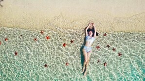 A person lying on a beach with clear water and starfish. - CALI PHU QUOC HOTEL (Phu Quoc)