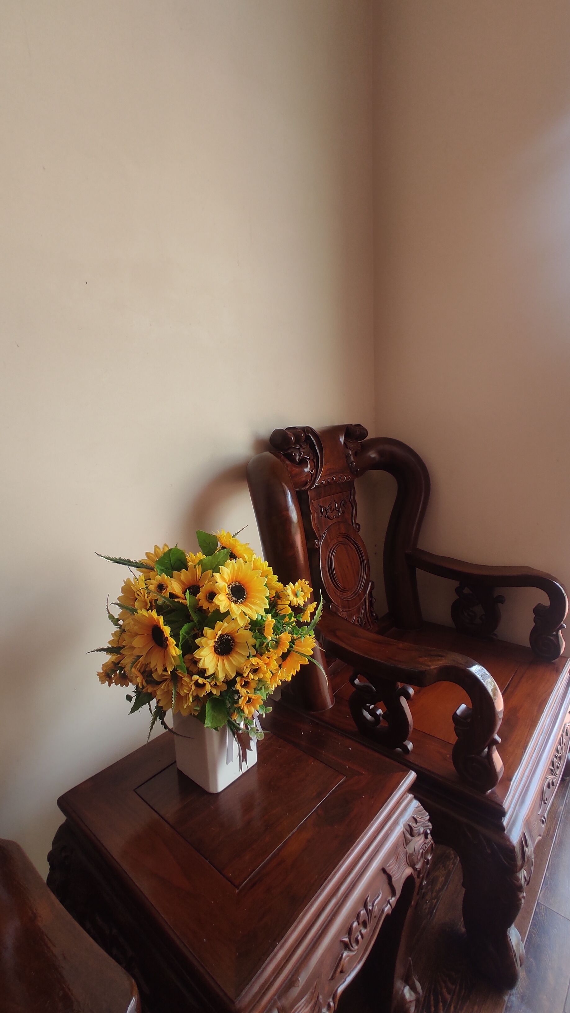 A wooden chair with intricate carvings and a vase of sunflowers on a wooden table.