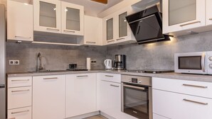 Moderni keittiö, jossa on valkoiset kaapit, sisäänrakennettu uuni, mikroaaltouuni ja kahvinkeitin.