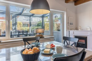 Enjoy meals at the dining table surrounded by comfortable chairs, with a fireplace in the background and a view of the neighborhood.