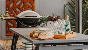 A table set for a meal with a grill, plates, glasses, and a bottle of liquor. - The Little Distillery - Beachside Pool Retreat (Safety Beach)