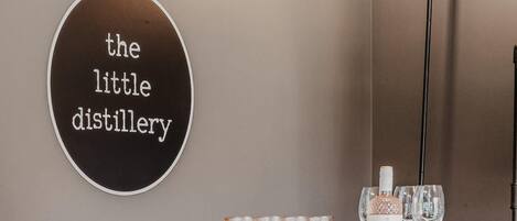 Una pared con un letrero que dice 'the little distillery' y una zona de bar con vasos y botellas.