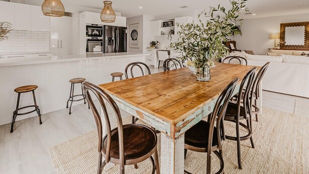A modern kitchen with white cabinetry, a wooden dining table, and hanging wicker pendant lights. - The Little Distillery - Beachside Pool Retreat (Safety Beach)