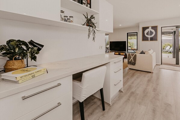 A modern kitchen with white cabinetry, a dining area with a white table and chairs, and a living room with a sofa and a TV.