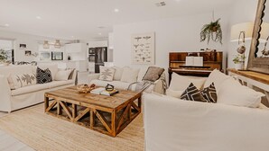 A modern living room with a sofa, coffee table, and piano. - The Little Distillery - Beachside Pool Retreat (Safety Beach)