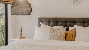 A bedroom with a large bed, a bedside table with a vase and books, a textured ceiling lamp, and a wall-mounted decor piece. - The Little Distillery - Beachside Pool Retreat (Safety Beach)