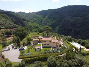 Une villa située sur une colline, dotée d’une piscine et entourée d’une végétation luxuriante, avec une chaîne de montagnes en toile de fond.