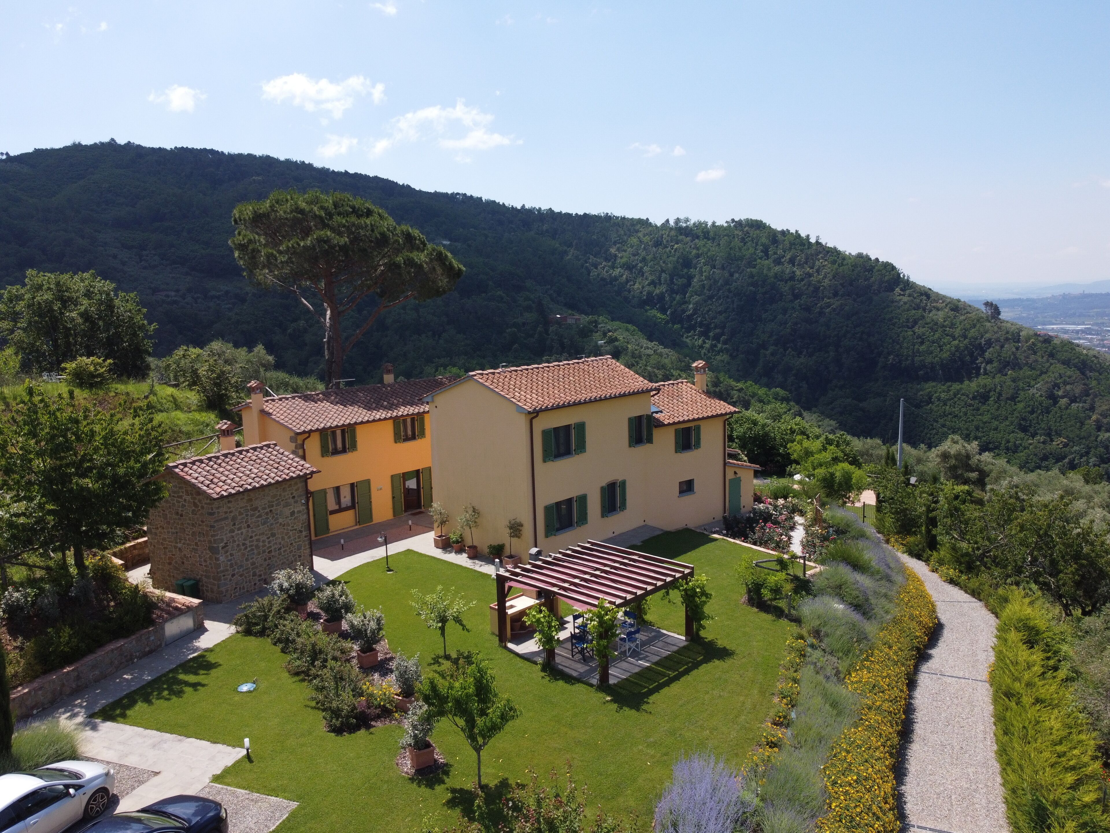 Une maison à deux étages avec un jardin, une pergola et une vue sur une colline.