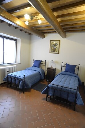 Une chambre avec deux lits, un radiateur, une fenêtre et un luminaire au plafond.