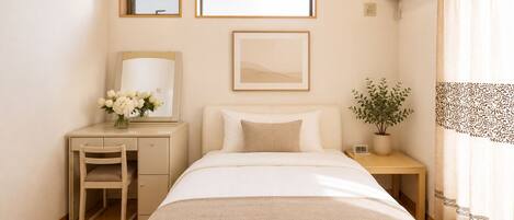 A hotel room with a bed, a desk, a chair, a potted plant, and a window.