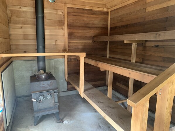 L’intérieur d’un chalet en bois, avec un poêle à bois, une marmite en métal posée sur le poêle et un banc en bois.
