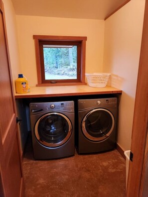 Une buanderie équipée de deux machines à laver à chargement frontal, d’une fenêtre et d’un panier à linge posé sur le plan de travail.