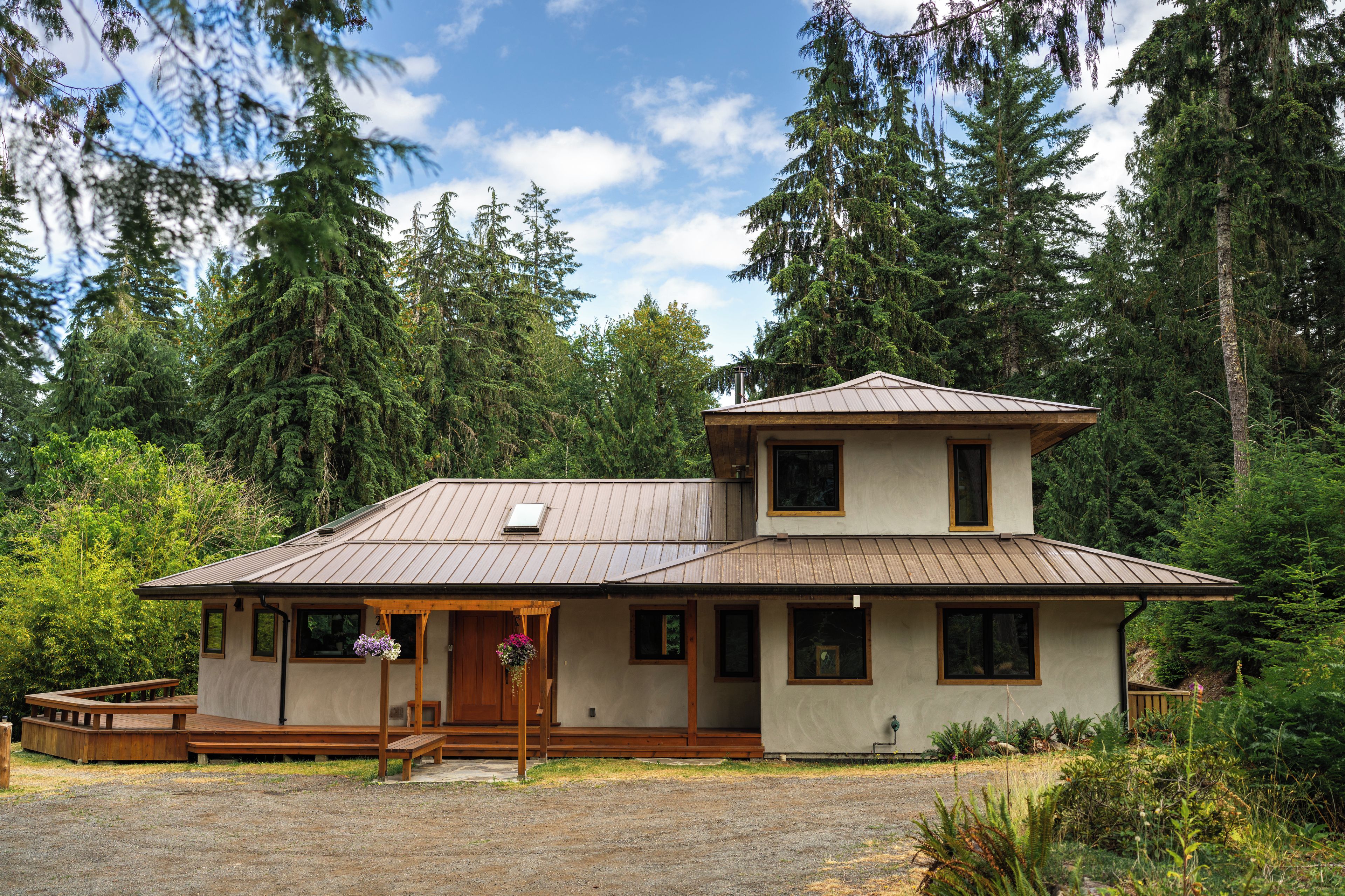 A two-story cabin with a metal roof, surrounded by dense forest.