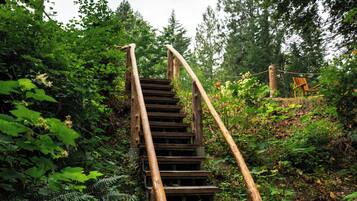 A wooden staircase leading up to a covered area, surrounded by dense greenery and trees.
