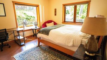A bedroom with a bed, a desk, a chair, a lamp, and a window with a view of greenery.