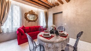 Un coin repas avec une table ronde dressée pour deux personnes, un canapé rouge et un lustre.