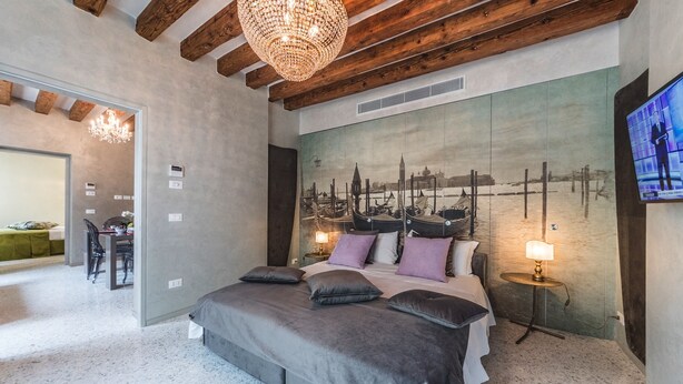 Une chambre avec un grand lit, une fresque représentant un paysage urbain sur le mur, un téléviseur et un lustre.