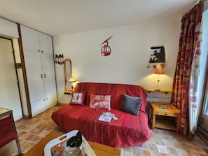 Ein gemütliches Zimmer mit einem roten Sofa, einem Holztisch, einem Spiegel und einem Kleiderschrank.