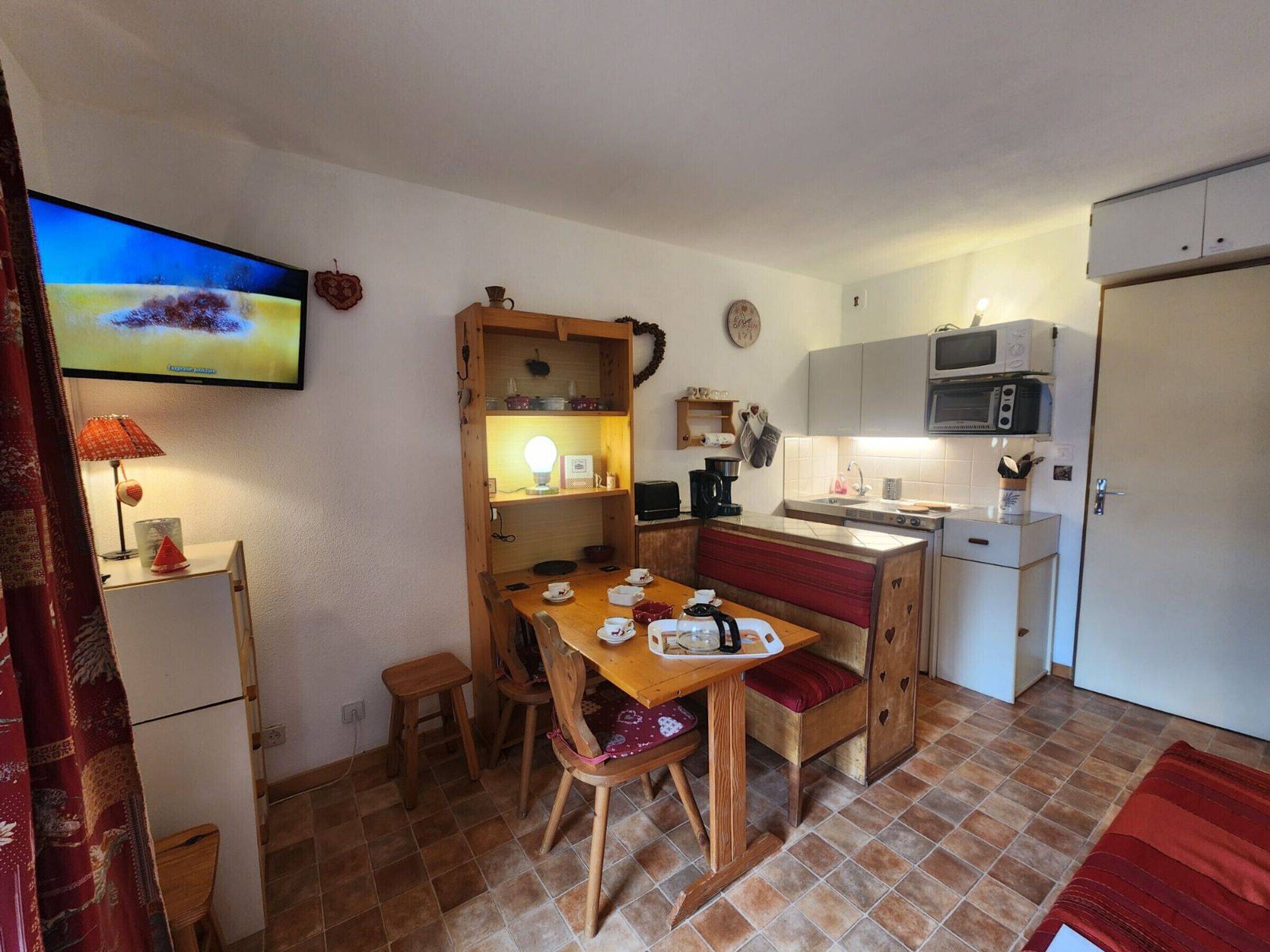 A compact kitchen with a dining table, chairs, a microwave, and a television.