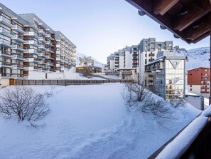 A snow-covered residential area with modern apartment buildings, a wooden fence, and bare trees.