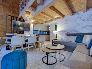 A modern interior with a dining area, kitchen, and living space, featuring wooden beams, a large TV, and a mountain-themed wall.