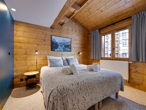 A bedroom with a wooden ceiling, a bed with a patterned blanket, two bedside lamps, a window with curtains, and a view of buildings outside. - Cozy duplex in the heart of Tignes Val Claret for 6 people (Tignes)