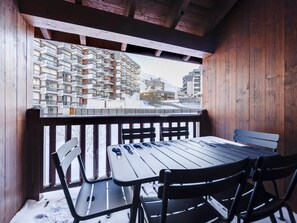 A wooden balcony with a table and chairs, overlooking a snowy mountain area with a multi-story building in the background. - Cozy duplex in the heart of Tignes Val Claret for 6 people (Tignes)