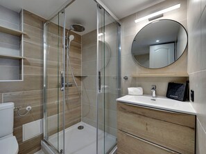 A modern bathroom with a glass-enclosed shower, a wooden vanity, and a round mirror.