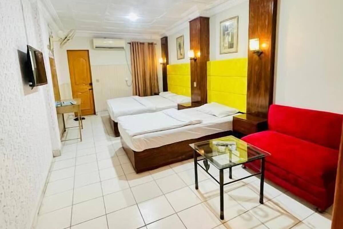 A hotel room with a bed, a red sofa, a glass coffee table, and a TV on the wall.
