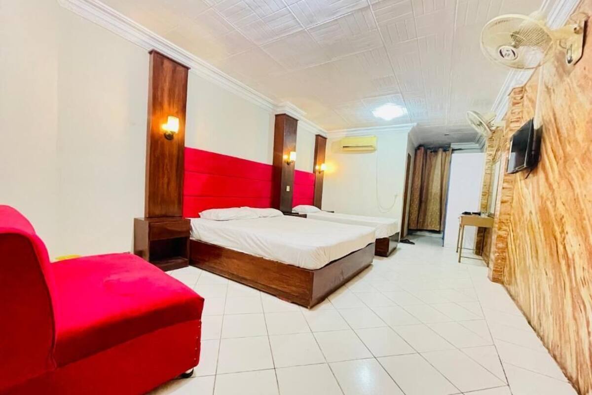 A hotel room with a large bed, a red sofa, and a wooden accent wall.
