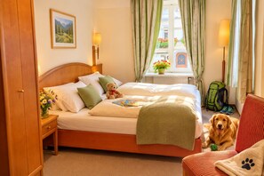 A hotel room with a bed, a teddy bear, a dog, a window with curtains, a lamp, and a painting on the wall. - FEWO Haus Gabi | Ski Holiday Murau | Sleeps 8 | Dogs | Kreischberg & Lachtal (Sankt Peter am Kammersberg)
