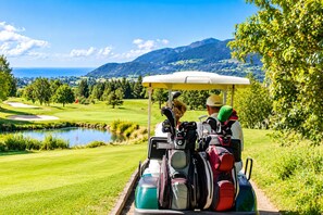 Un carrito de golf en un campo de golf con un lago y montañas al fondo.