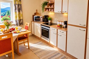 Una cocina compacta con microondas, horno y cafetera, una mesa de comedor con alimentos para el desayuno, y vistas al exterior a través de una ventana.