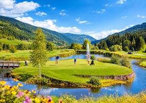 A golf course with a pond, surrounded by hills and trees.