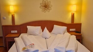 A neatly made bed with white linens and towels, two bedside lamps, and a decorative wall piece.