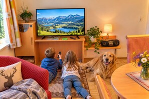 A living room with a television displaying a scenic landscape, a dog lying on the floor, and a child playing with a remote control. - FEWO Haus Gabi | Ski Holiday Murau | Sleeps 8 | Dogs | Kreischberg & Lachtal (Sankt Peter am Kammersberg)