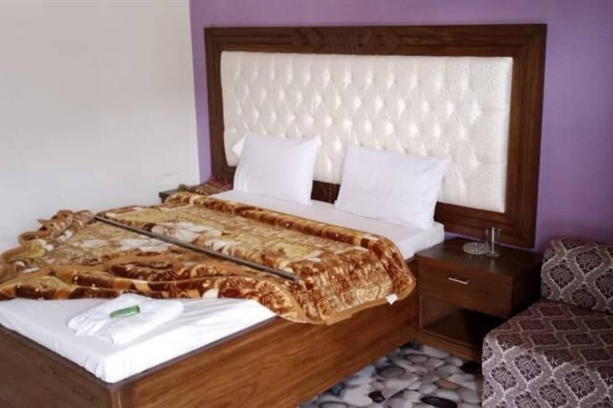 A neatly made bed with a patterned blanket, a wooden headboard, a nightstand with a lamp, and a patterned sofa.